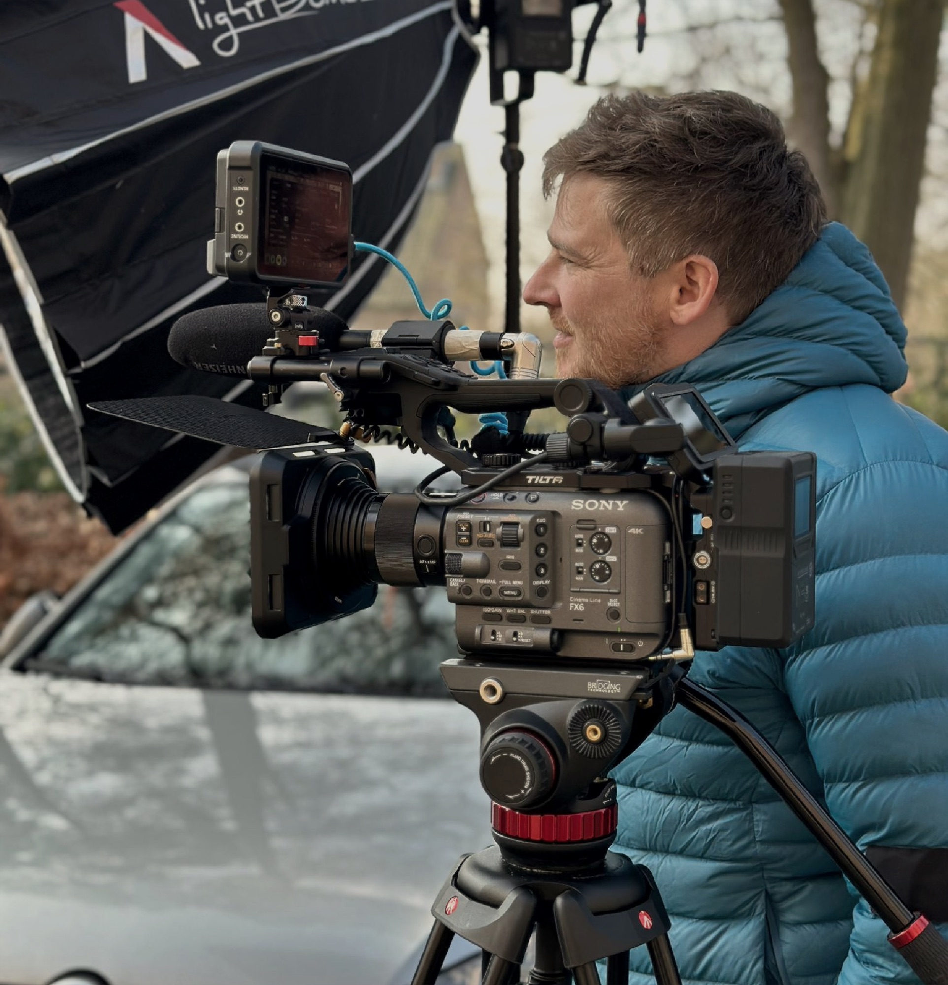 Lars behind a cinema camera on a tripod, filming outdoors